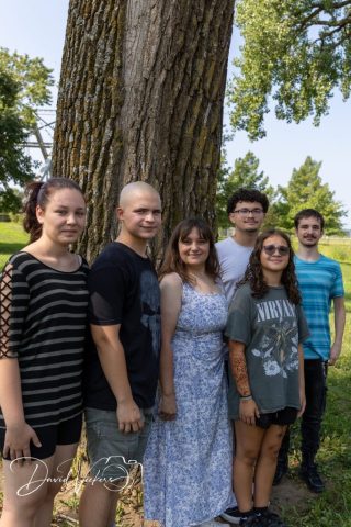 Young Adults in the Park Five young adults standing close together under a wide shade tree in a green park
