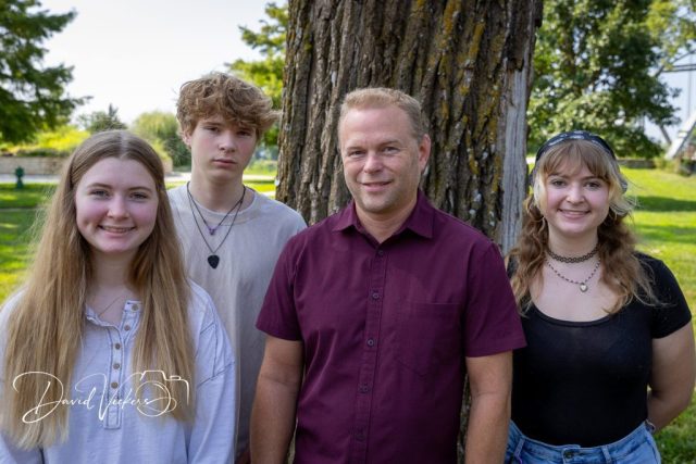 Dad and His Three Kids A father in a maroon shirt with his three teenage children beneath a shade tree
