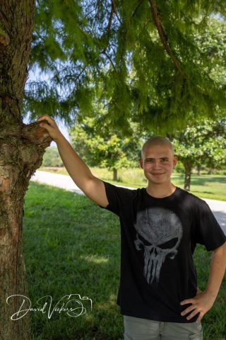 Teen Leaning Against a Tree Teenage boy in a graphic tee leaning against a tree trunk in a sunlit park