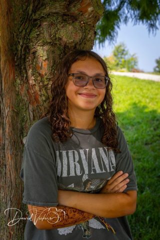 Smiling Portrait Under the Tree Teenage girl in glasses with arms crossed, smiling in front of a textured tree trunk