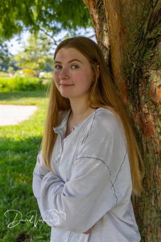 Quiet Portrait in Natural Light Young woman with long red hair resting against a tree, backlit by soft afternoon sun