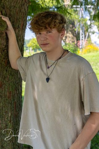 Casual Outdoor Portrait Teenage boy resting one hand on a tree trunk, looking off camera in warm natural light