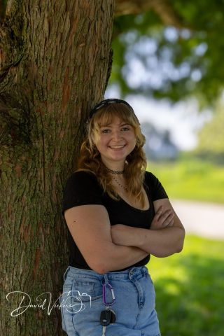 Bright Smile in the Park Young woman in a black top with arms crossed, laughing against a tree in a green park