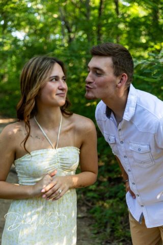 1g2a5036 Engaged couple face to face in the woods as he leans in to kiss her
