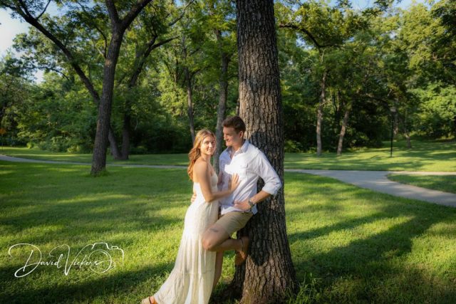 1g2a5071 Engaged couple leaning against a large tree in a sunlit park