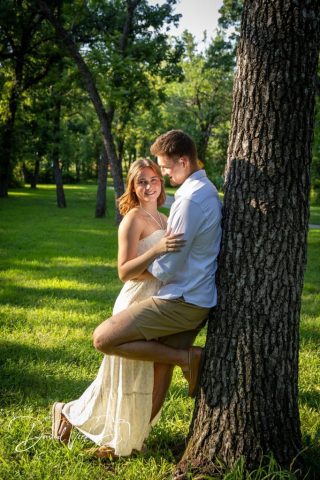 1g2a5109 Engaged couple embracing beside a large tree trunk in a shady park