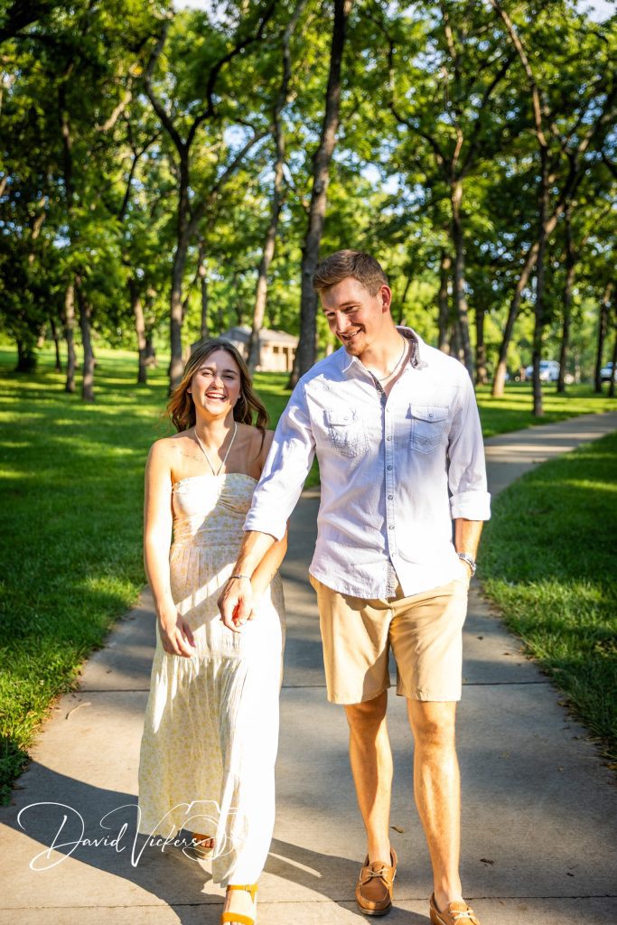 Engagement Photography Engaged couple walking hand in hand down a tree-lined path in a Kansas City park