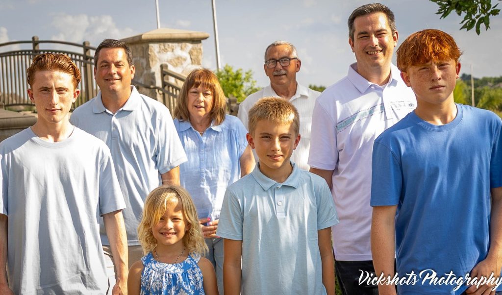 Family Photographer in Overland Park, KS Extended family of nine in coordinated blue standing together on a sunny summer afternoon