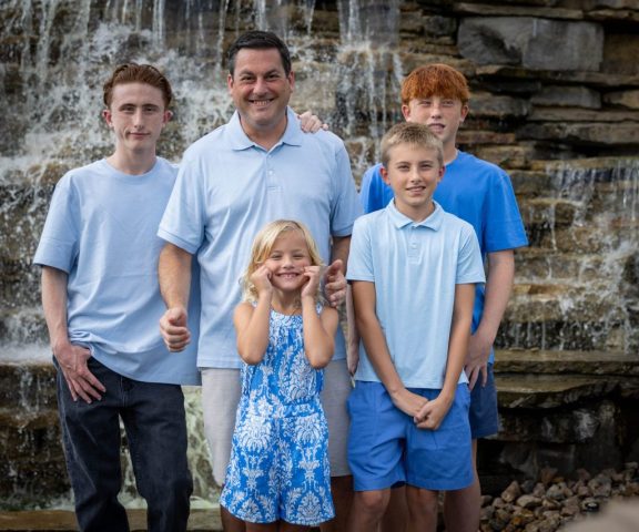 Family of Five at the Waterfall Father with his four children in coordinated blue in front of a cascading stone waterfall