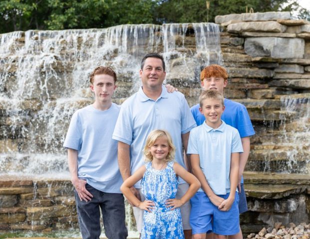 Family in Front of the Falls Family of five posed in front of a wide stone waterfall on a summer day