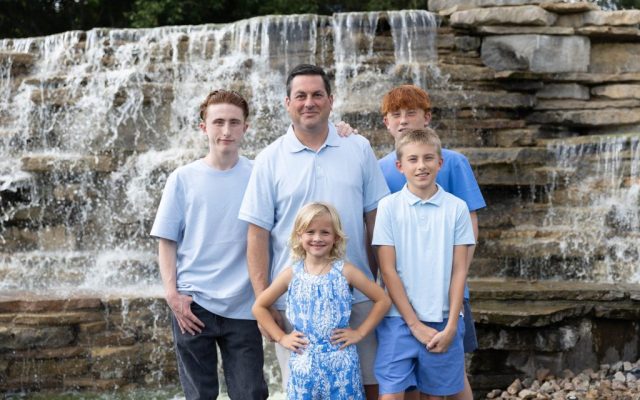 Siblings and Dad by the Water Father and four children standing together in front of a layered rock waterfall