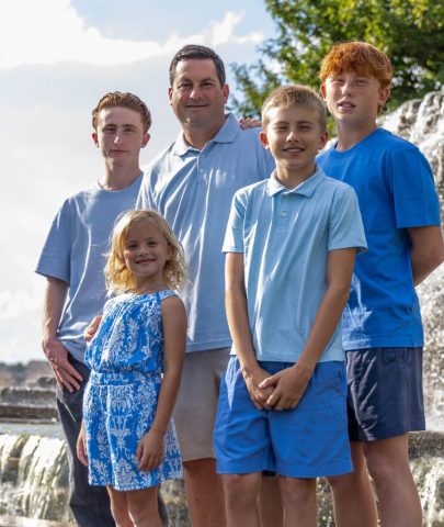 Family Portrait in Afternoon Light Father with his four children standing together beside a waterfall under a blue sky
