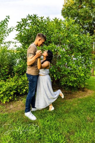 engagement photos by the lake Fiance lifting his fiancee off her feet in a grassy clearing