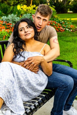 engaged couple on a park bench Engaged couple sitting together on a park bench in front of a flower bed