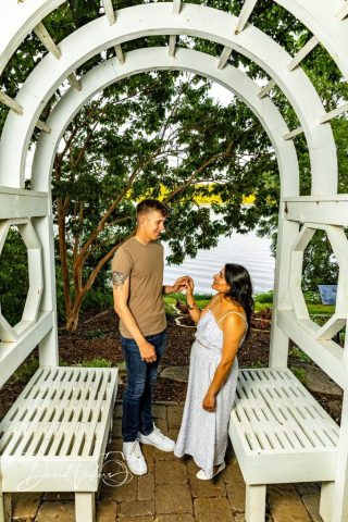 engagement photos at the white garden arbor Engaged couple holding hands beneath a white wooden garden arbor