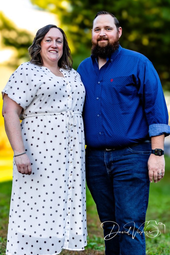 Smiling couple standing arm in arm on a lawn in golden evening light