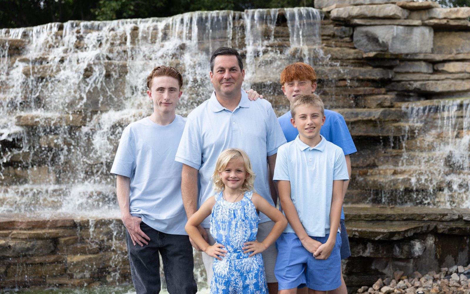 Family in light blue posing beside a cascading waterfall in natural light