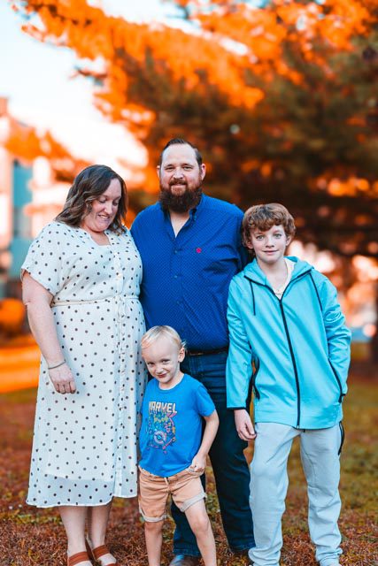 Fall Family Photos in Kansas City Mom, dad and two boys standing together in front of golden fall foliage